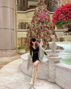 Photo of a young woman sitting in front of a Christmas tree, next to a fountain, sent by the WhatsApp scammer.