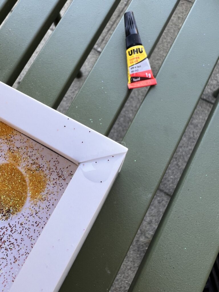 a photo of a superglue packet and a corner of a macbook pro box. There is a puddle of glue on the corner where the box cover will touch it once closed