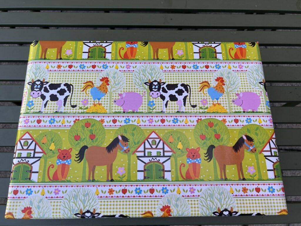 photo of a box wrapped in colorful wrapping with cows, chickens, cats, pigs, roosters, trees and houses on it