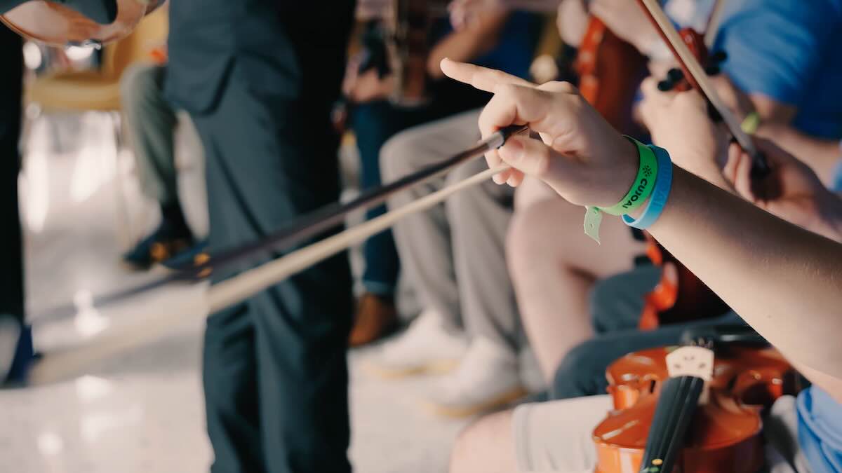 Video preview image. A raised hand with a CUJO AI bracelet holds a violin bow. In the background, a violin is visible